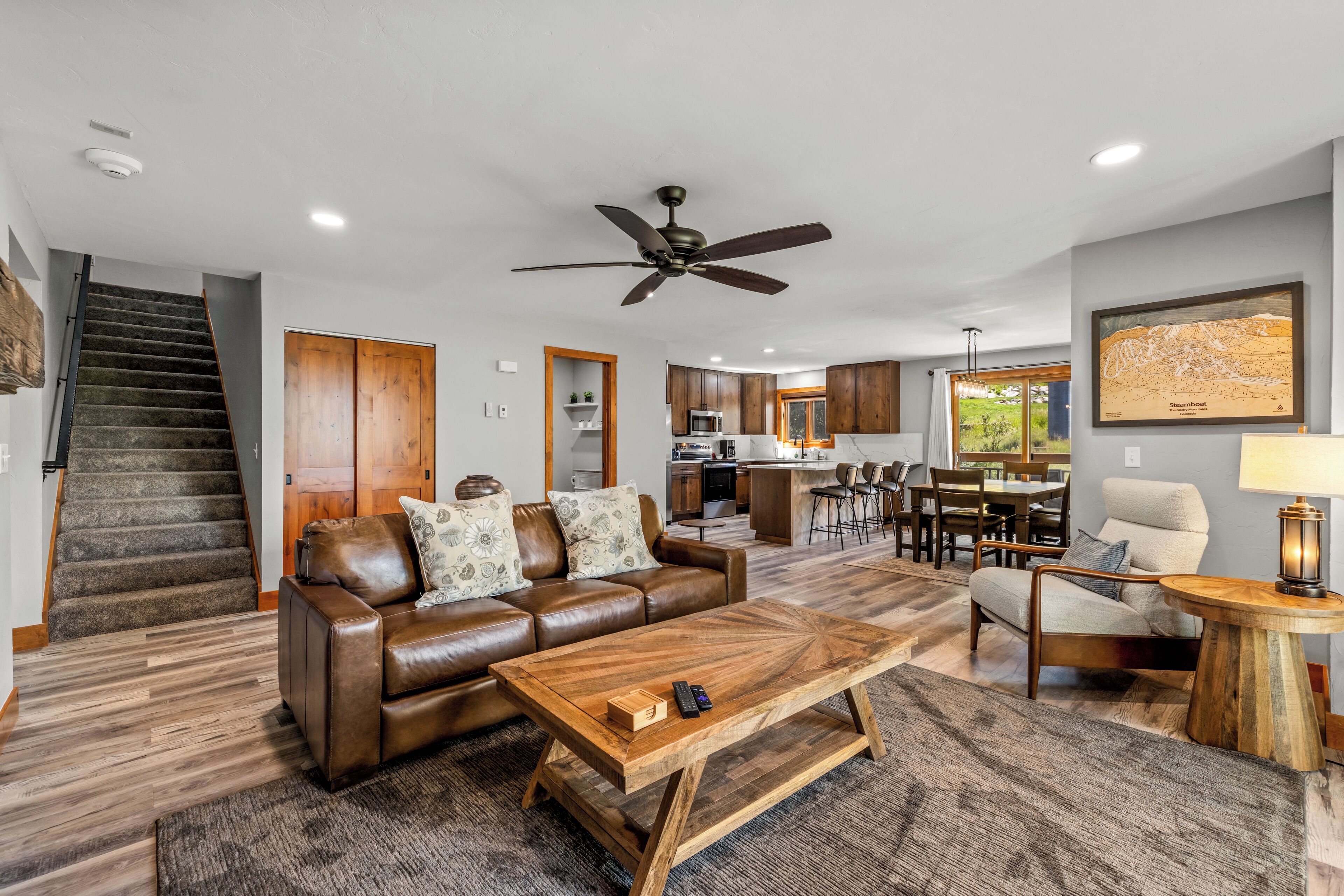 A modern living room with a leather sofa, wooden coffee table, and a dining area with a kitchen in the background.