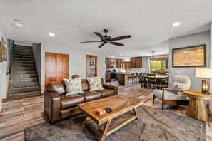A modern living room with a leather sofa, wooden coffee table, and a dining area with a kitchen in the background.