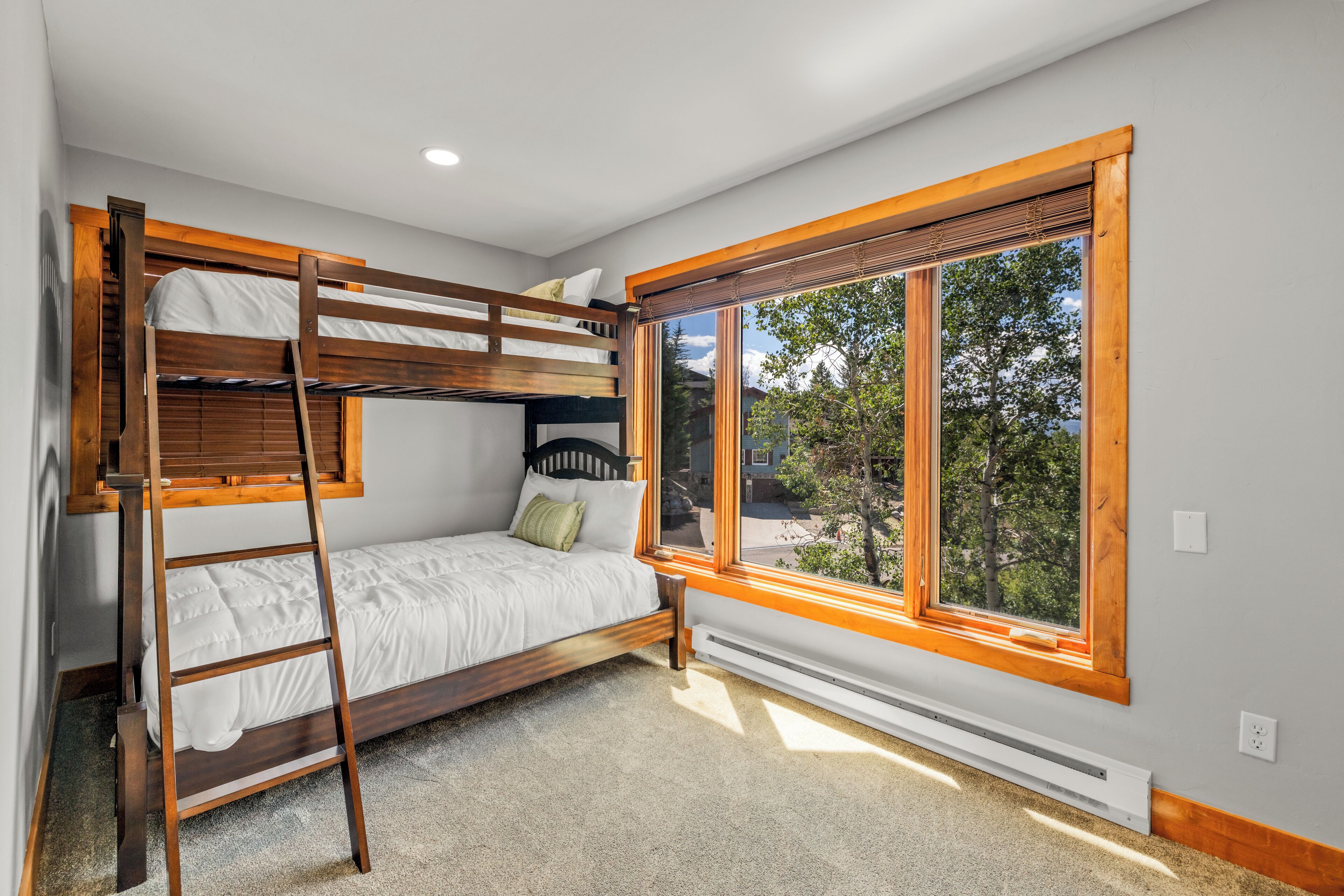 A bunk bed room with a ladder, a window with a view of trees, and a thermostat on the wall.