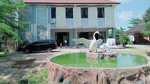 Un bâtiment à deux étages, doté d’un toit recouvert de tuiles rouges, d’une enseigne indiquant « SMK PK » et d’un petit étang orné de sculptures de cygnes.