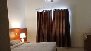 Une chambre d’hôtel avec un lit, une table de chevet avec une lampe, une fenêtre avec des rideaux et un appareil de climatisation fixé au plafond.