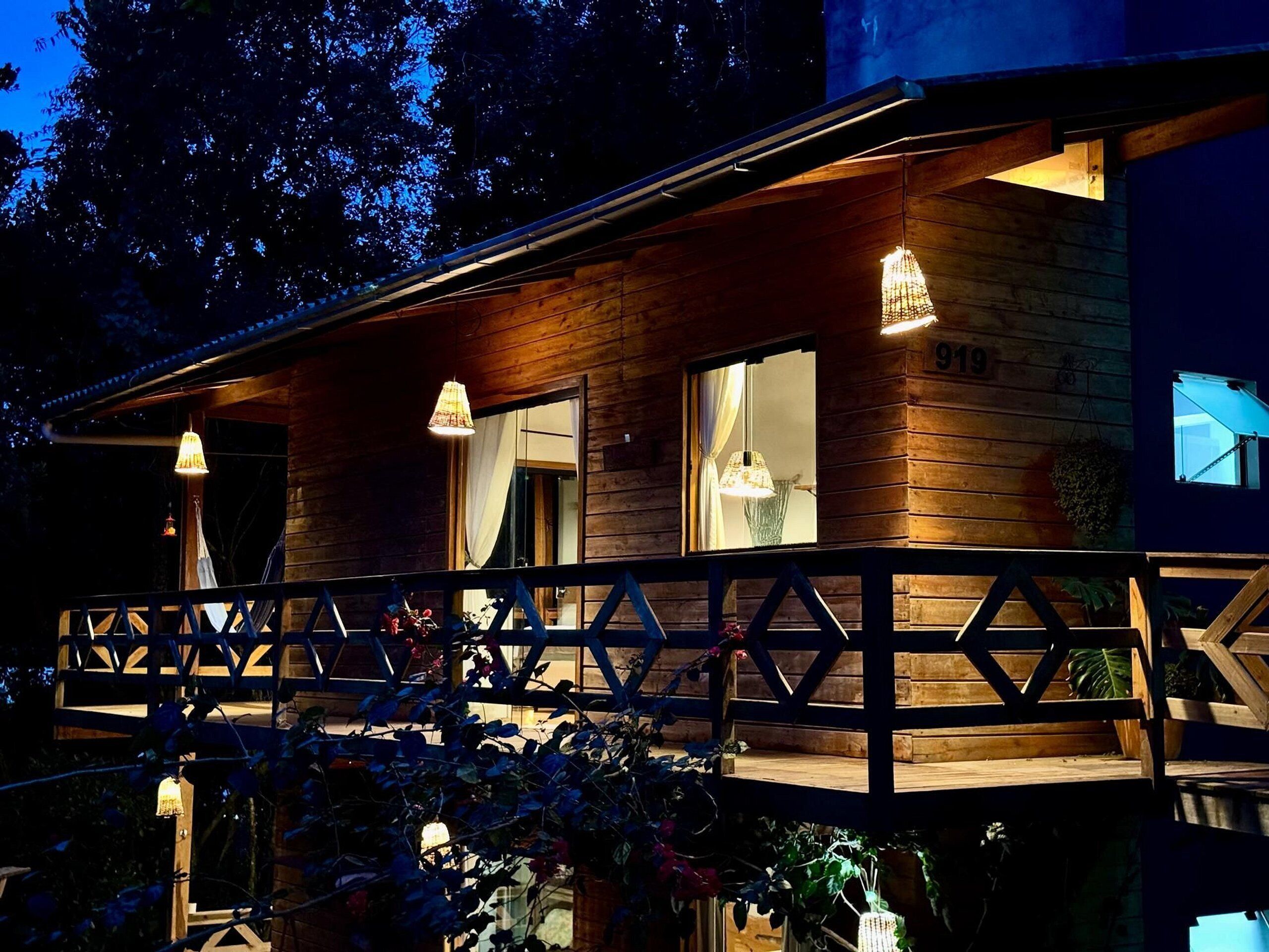 A wooden cabin with a balcony, large windows, and hanging lights.