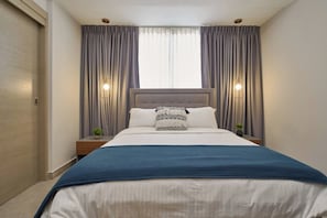 A bedroom with a bed, curtains, bedside lamps, and a window.
