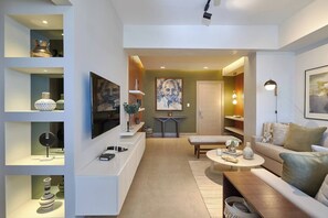 A modern living room with a flat-screen TV, a coffee table, a sofa, and a dining area with a table and chairs.