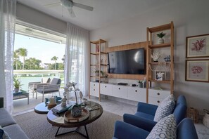 A modern living room with a flat-screen TV, a sofa, a coffee table, and a balcony with outdoor furniture.