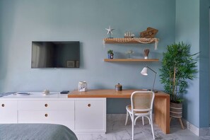 Ein modernes Schlafzimmer mit Bett, Schreibtisch, Sessel, Fernseher, einer Ablage mit Dekoration und einer Topfpflanze.