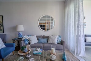 Ein Wohnzimmer mit grauem Sofa, blauem Sessel, rundem Spiegel und Couchtisch mit Dekoration.