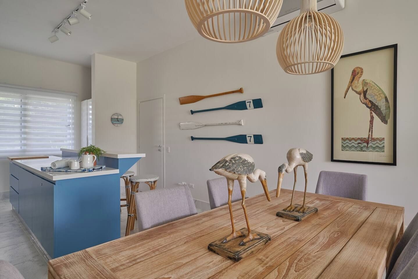 A modern kitchen with a blue island, wooden dining table, and decorative bird sculptures.