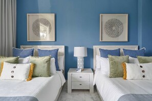 A hotel room with two beds, a nightstand with a lamp, and two wall-mounted artwork pieces.