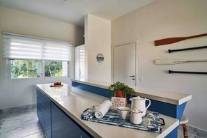 A kitchen with a marble floor, a window with blinds, a counter with kitchenware, and a door with a clock.