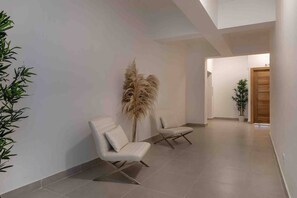 A hallway with two white chairs, a tall decorative plant, and a wooden door at the end. - ®{LUX~City~Skyline} @DowntownSD PrivéJaccuzi+Gym (Santo Domingo)