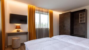 A hotel room with a bed, a TV mounted on the wall, a desk with a lamp, and a wardrobe. - Lorenzhaus Exclusive Residence: Deluxe apartment with 3 bedrooms (Sankt Lorenz)