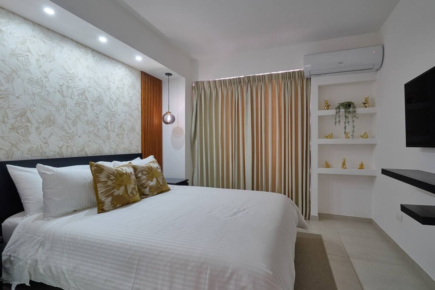 Un dormitorio moderno con una cama grande, un televisor montado en la pared y un estante empotrado con objetos decorativos.