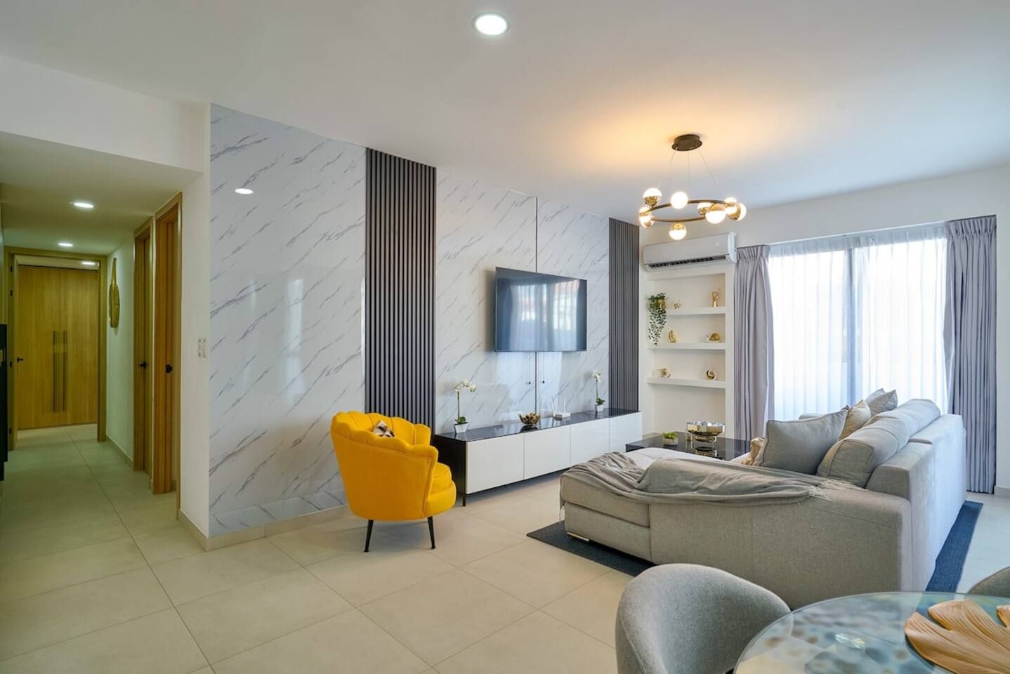 A modern living room with a sofa, a yellow chair, a TV, and a glass coffee table.