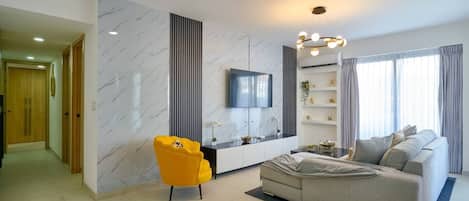 A modern living room with a sofa, a yellow chair, a TV, and a glass coffee table.