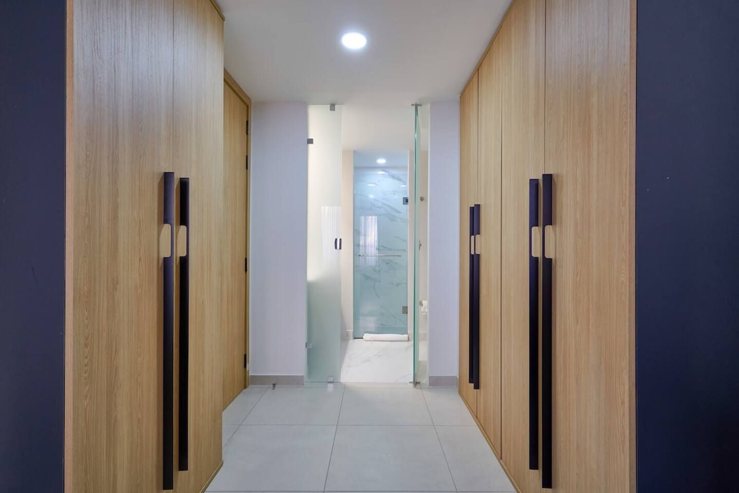 Un pasillo con paneles de madera y suelo de baldosas, que conduce a una puerta de cristal.