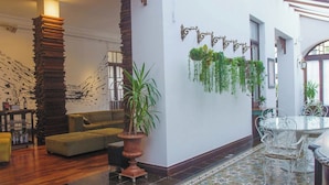 Een ruime lobby met een hoge houten pilaar, een groene bank, een patroon vloer en hangende planten.