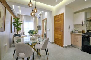 Un salon moderne avec une table à manger en verre, deux chaises, une plante en pot et une porte en bois.