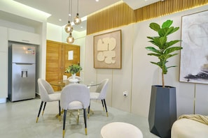A modern kitchen with a stainless steel refrigerator, a glass dining table with four chairs, and a potted plant.
