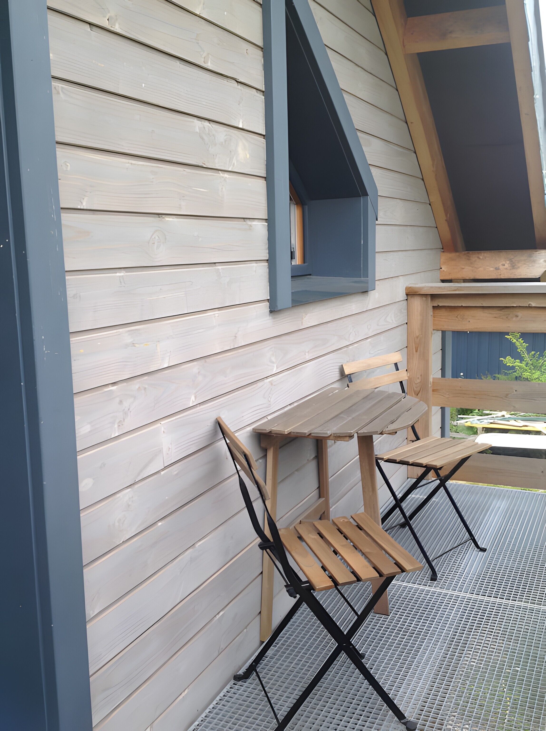 En träveranda med ett bord och stolar, ett blått solskydd och ett nät som golv.
