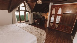 A bedroom with a large bed, wooden flooring, a TV, and a wardrobe.