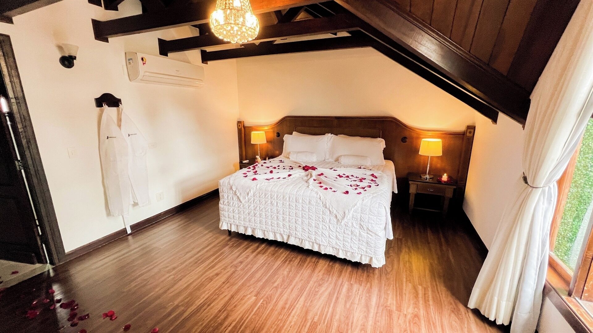 A bedroom with a wooden ceiling, a bed with white bedding, two bedside lamps, and a window with curtains.
