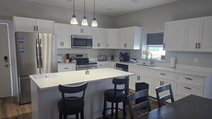 A modern kitchen with white cabinets, stainless steel appliances, a central island with bar stools, and pendant lighting. - 3-bedroom Condo 5127 C ADA (Bellaire)