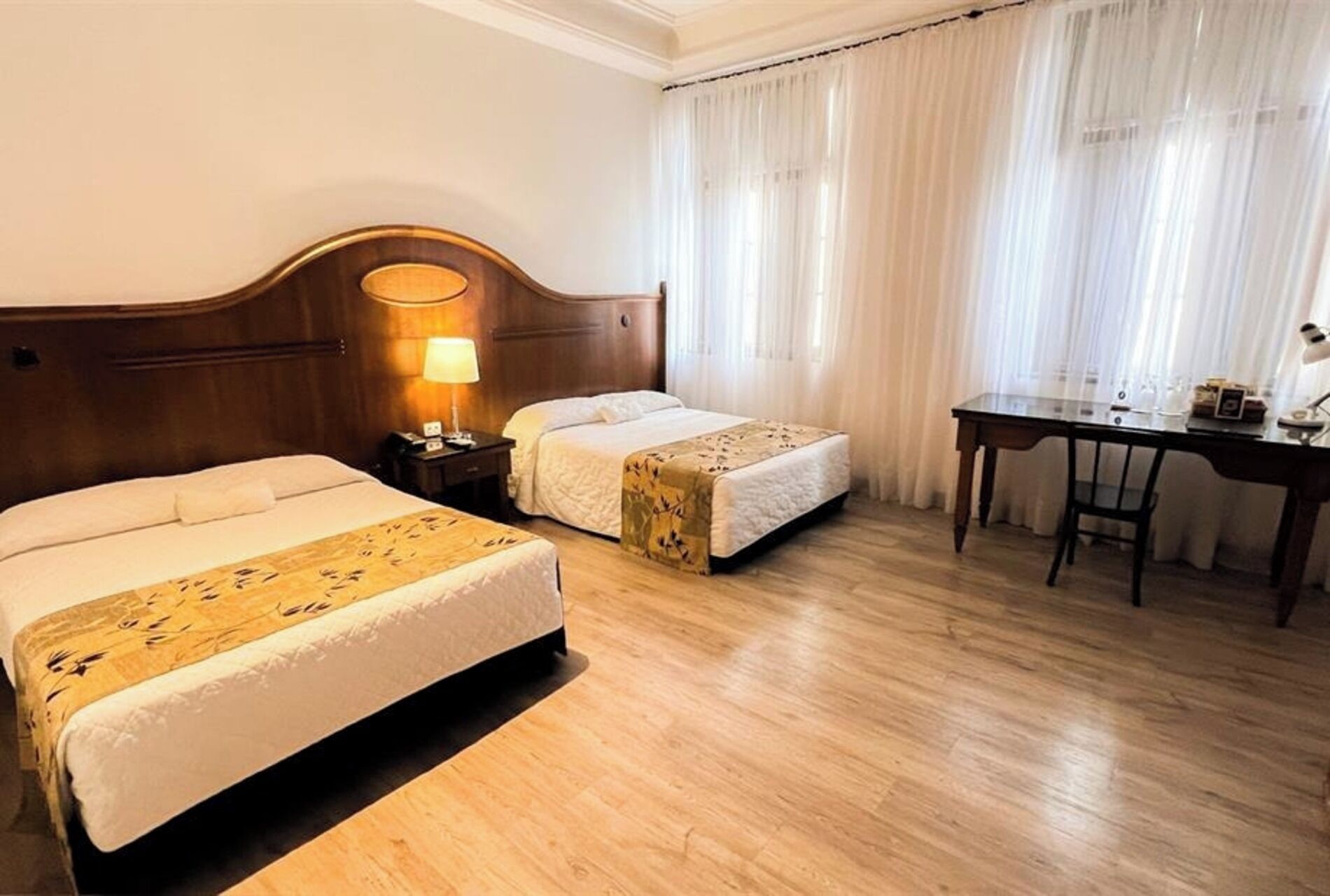 A hotel room with two beds, a desk, and a lamp.
