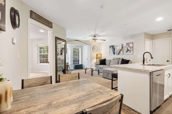 A modern kitchen with a central island, a dining area with a wooden table, and a living room with a sofa and coffee table.