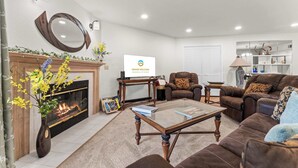 Ein Wohnzimmer mit Kamin, einer Couch, einem Couchtisch und einem Fernseher, der 'GRAND WELCOME' anzeigt.