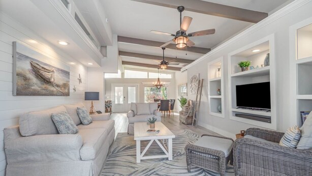 A spacious living room with a white sofa, a coffee table, wicker chairs, and a television mounted on the wall. - Villa Palma Encantada Gulf Access & Pet Friendly (Cape Coral)