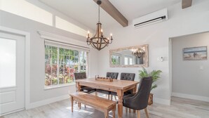 A dining area with a wooden table, chairs, a bench, a chandelier, a large window, and a mirror on the wall. - Villa Palma Encantada Gulf Access & Pet Friendly (Cape Coral)