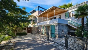 Ein modernes, zweistöckiges Haus mit einer Naturstein-Fassade, einer Holz-Pergola und einer Treppe, die zum oberen Geschoss führt.