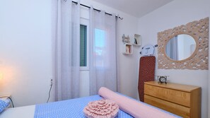 A bedroom with a bed, a wooden dresser, a mirror, and a window with curtains.