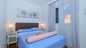 A bedroom with a bed, two bedside lamps, a nightstand, a window with curtains, and a wall painting. - Villa Hemingway beachfront by Villas Guide (Karlobag)