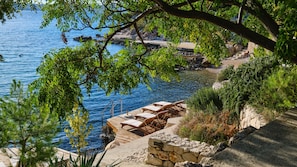 A coastal view with a wooden deck, lounge chairs, and a stone wall.