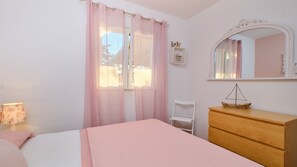 Une chambre à coucher avec un lit, une commode, une chaise, un miroir et une fenêtre avec des rideaux.