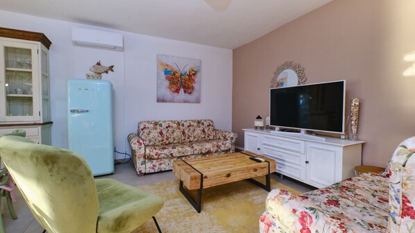 A living room with a vintage refrigerator, floral sofa, wooden coffee table, and a flat-screen TV on a white cabinet.