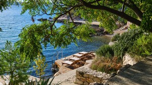 A coastal view with a wooden deck, lounge chairs, and a stone wall.