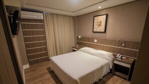 Habitación de hotel con cama, mesita de noche, lámpara, equipo de aire acondicionado y un cuadro en la pared.