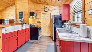 Cocina de cabaña de madera con techo de madera, armarios rojos, un refrigerador negro, una estufa y un microondas.