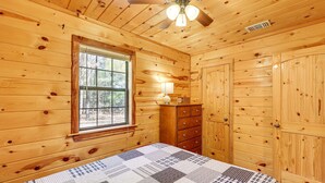 Un dormitorio de cabaña de madera con cama, cómoda y ventana.