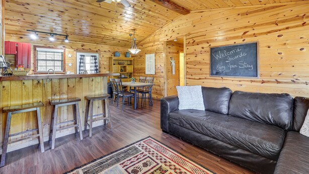 Interior de una cabaña de madera con barra, mesa de comedor y sofá de cuero.