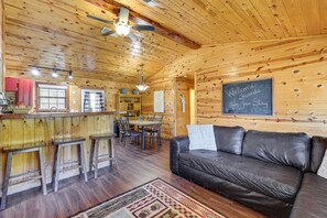 A wooden cabin interior with a bar area, a dining table, and a leather sofa. - Riverfront Fishing Cabin | 3BR Sleeps 6 | Great Weekday Rates (Broken Bow)