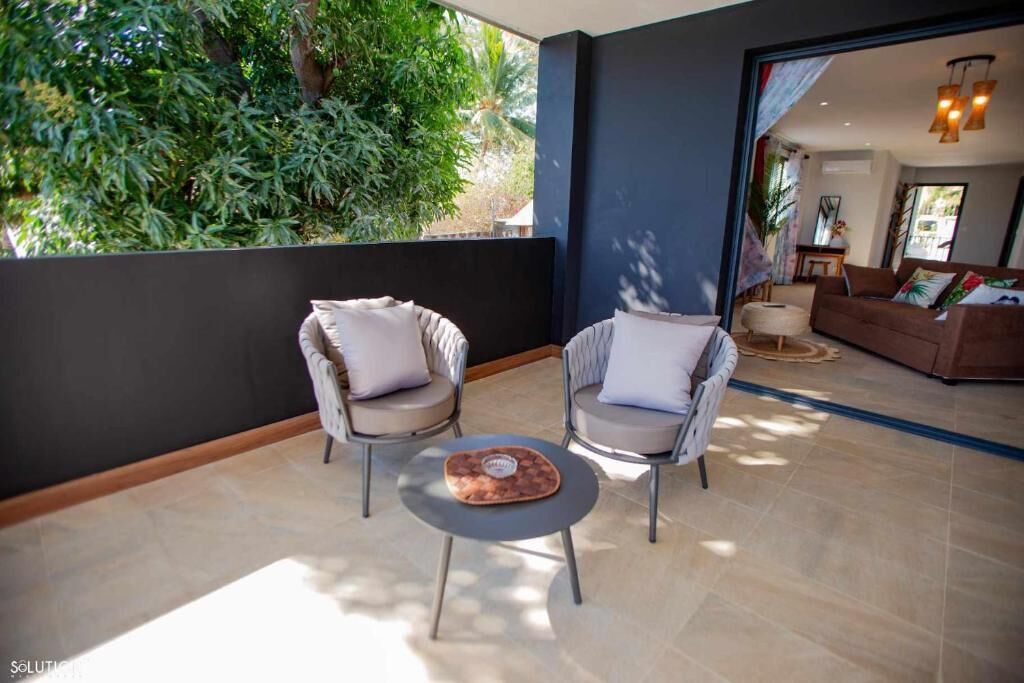 A modern living room with a sofa, two armchairs, a coffee table, and a view of greenery outside.