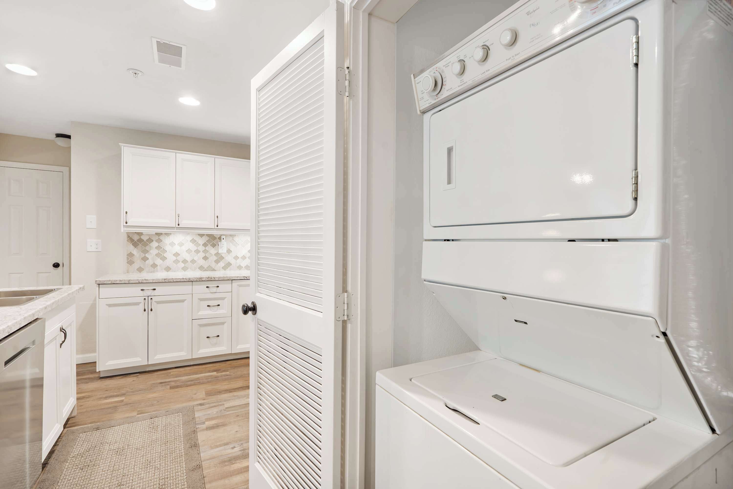 A laundry room with a stacked washer and dryer, white cabinets, and a patterned backsplash.