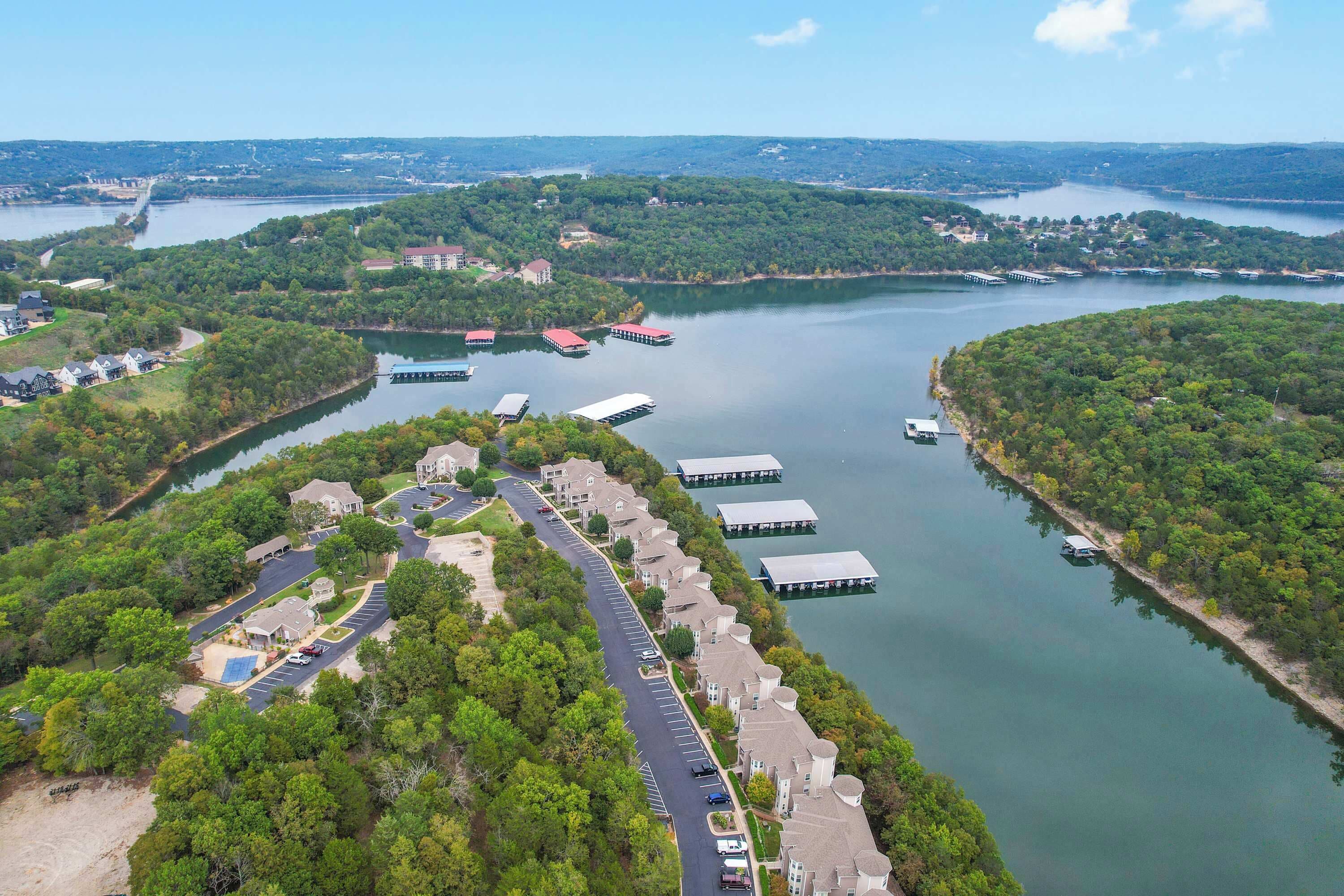 An aerial view of a lakeside residential area with docked boats, a marina, and a row of houses along the water's edge.