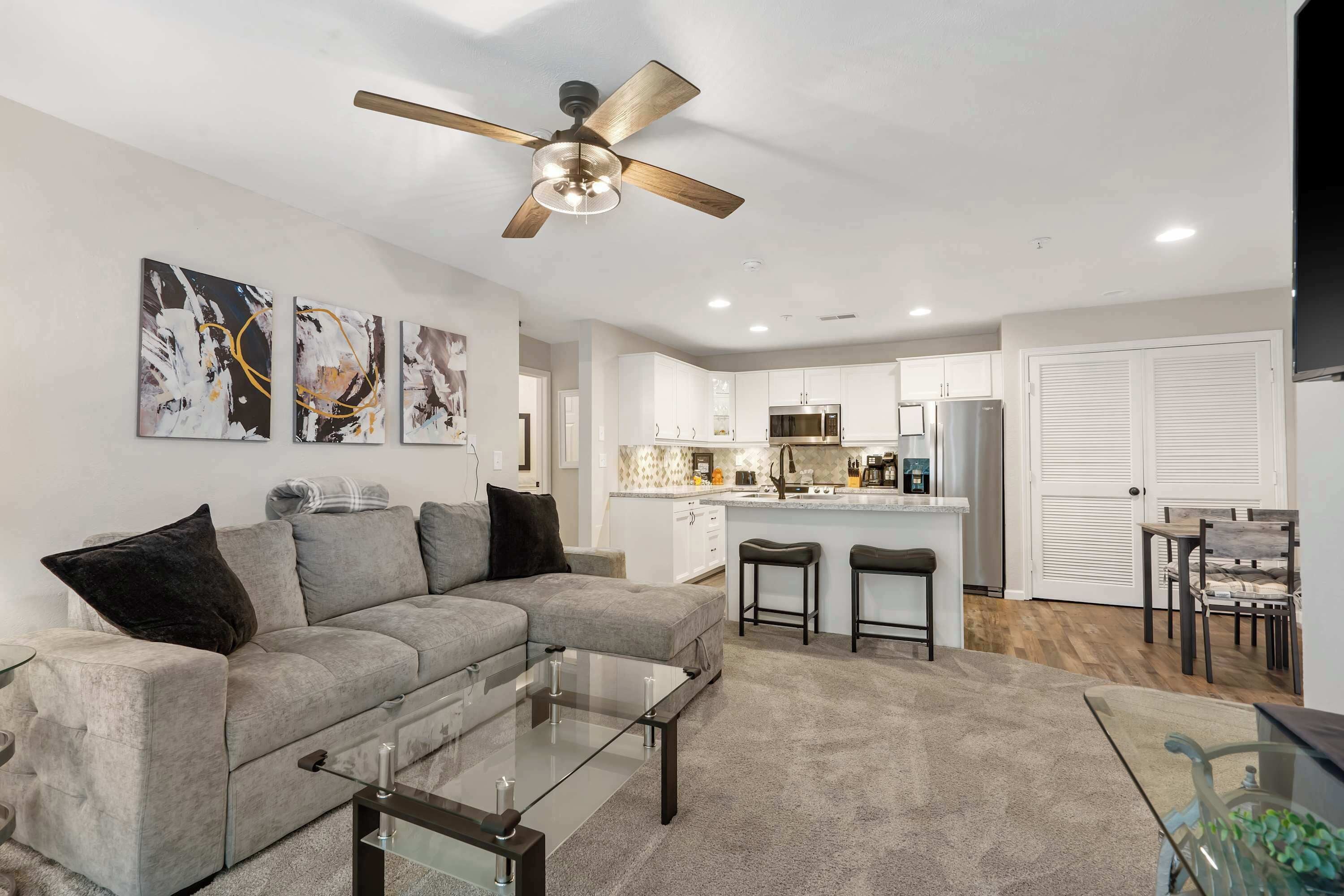 A modern living room with a grey sectional sofa, a glass coffee table, and a ceiling fan.