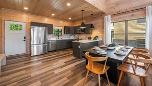 A modern kitchen with wooden floors, stainless steel appliances, and a central island with seating. - Modern Smoky Mountain Cabin Near Dollywood – Indoor Pool, Hot Tub & Arcade Fun (Pigeon Forge)