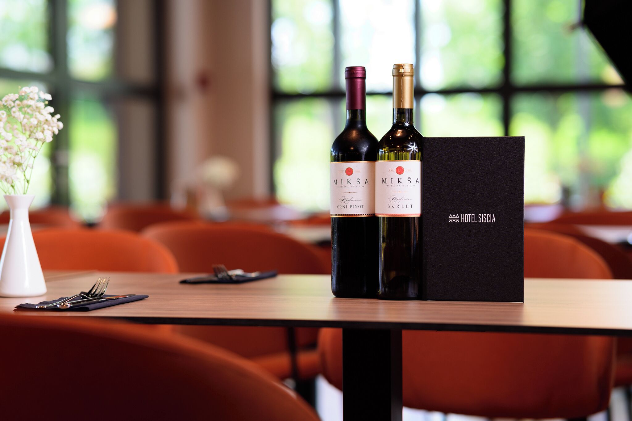Two bottles of wine and a black menu on a table in a restaurant.